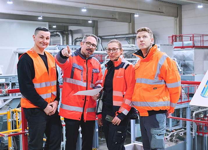 Vier Mitarbeitende besprechen Arbeitsabläufe in der Batterierecycling-Anlage in Ginsheim-Gustavsburg vor der modernen Sortiertechnik. © 2026, Saubermacher, Andre Dallavalle